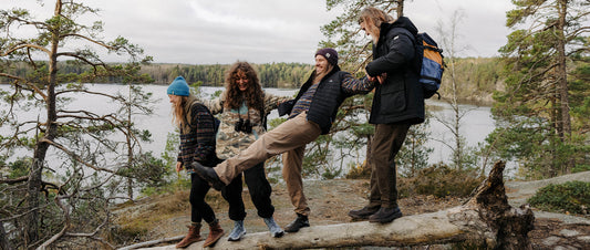 Four people stood on a log laughing, lake behind